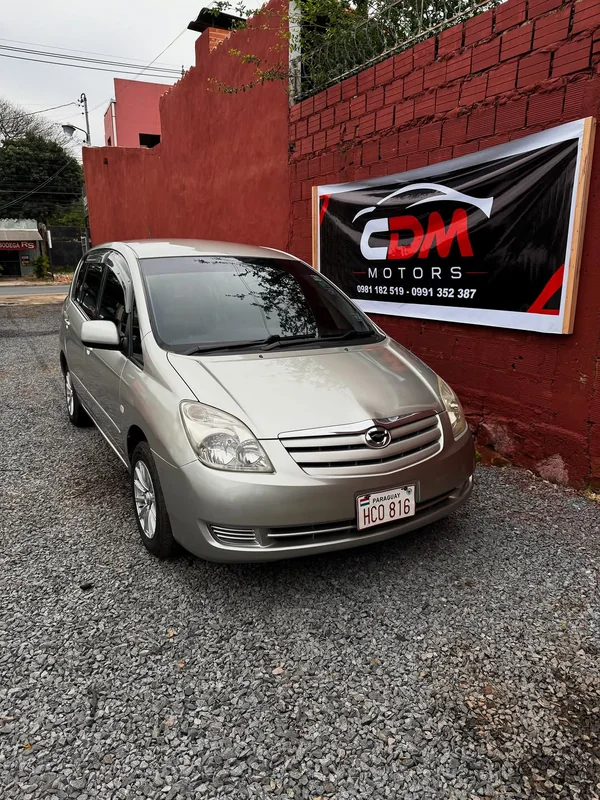 Toyota Spacio en el lote de ripio de CDM Motors, con el cartel en la pared